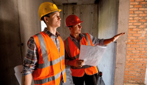 Construction manager and engineer dressed in orange work vests and helmets work with construction